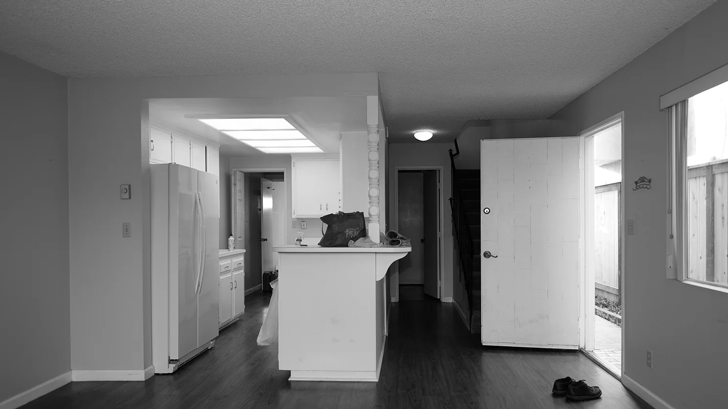 Existing kitchen with original galley style layout, framed cabinetry, and dropped ceiling with fluorescent lighting.